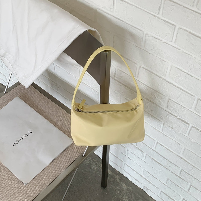 Pale yellow nylon shoulder bag hanging from chair frame against white brick wall