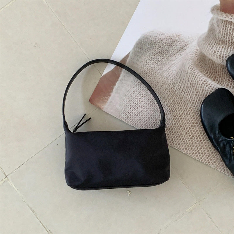 Black minimalist square nylon shoulder bag resting on beige floor tiles