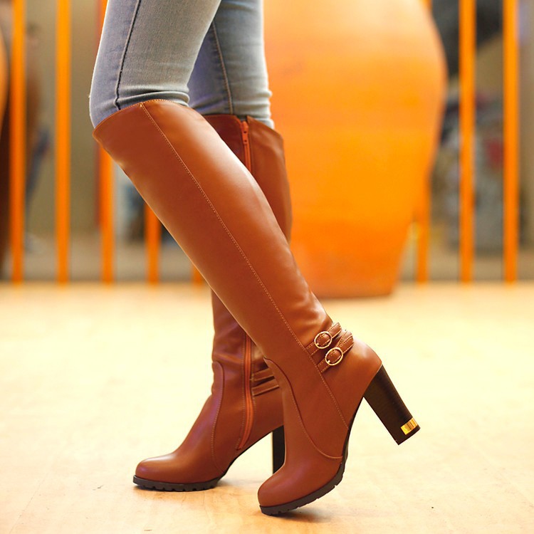 Brown Manhattan buckled knee-high boots styled with light-wash jeans, showing the side zipper and block heels.