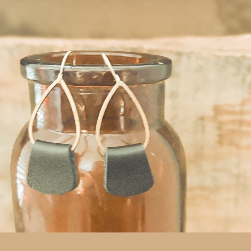 Black leather drop earrings with silver teardrop frames hanging from amber bottle