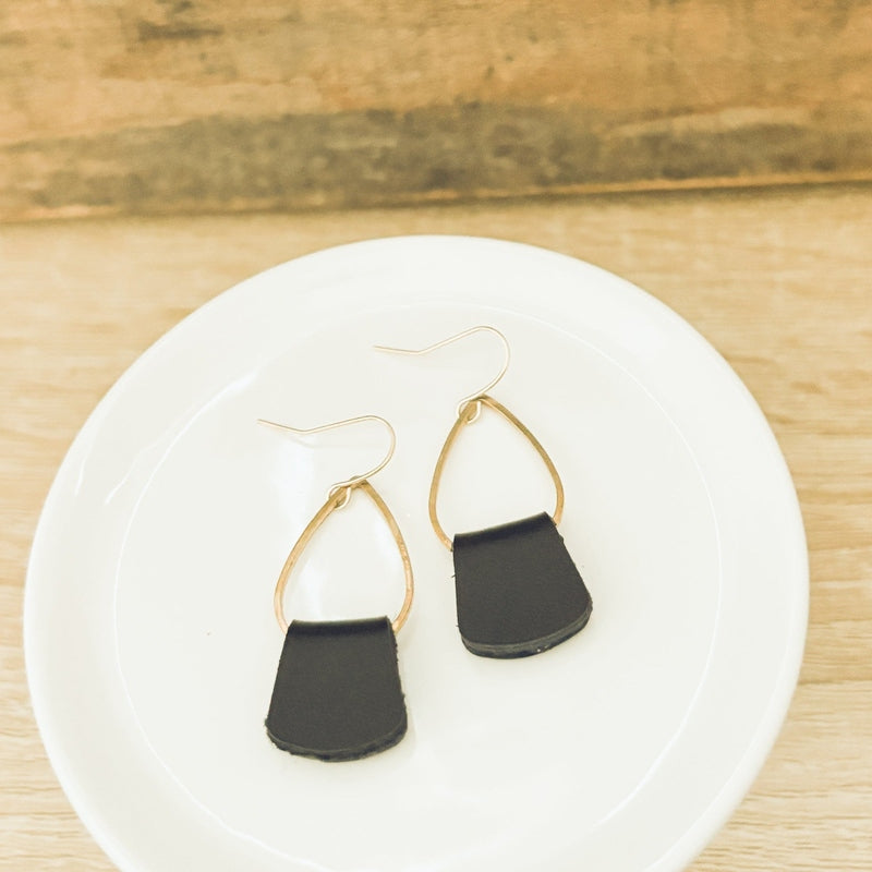 Dainty boho black leather drop earrings with gold teardrop frames on white plate