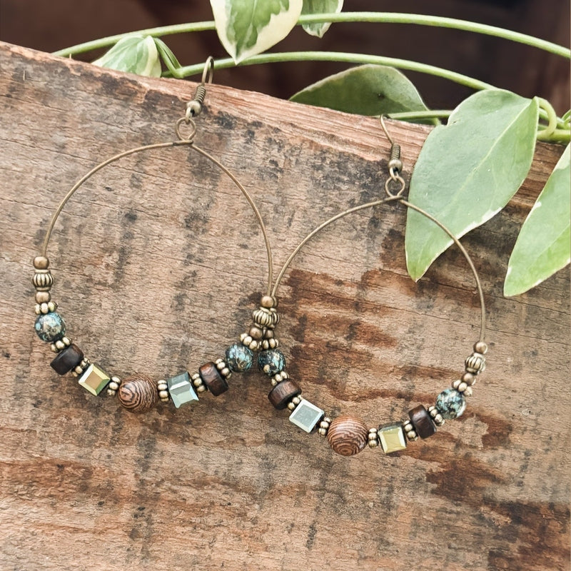 Large boho hoop earrings with mixed earth tone beadwork over rustic wood