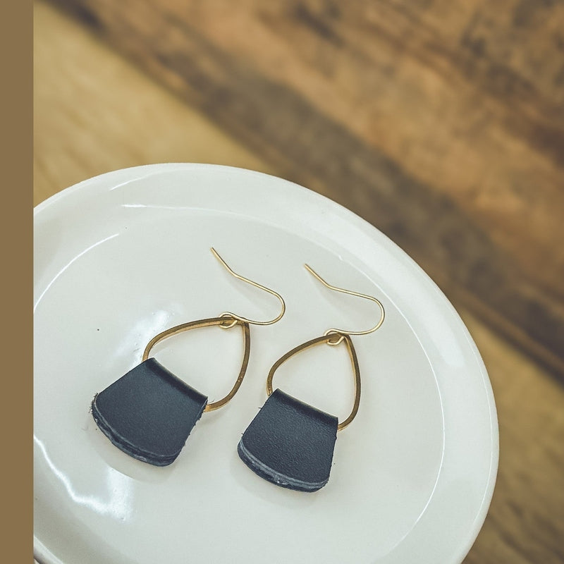 Black leather drop earrings with gold frames lying on white dish
