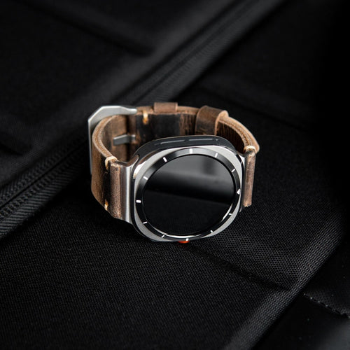 Full profile of brown leather watch band arranged in circle on black bag