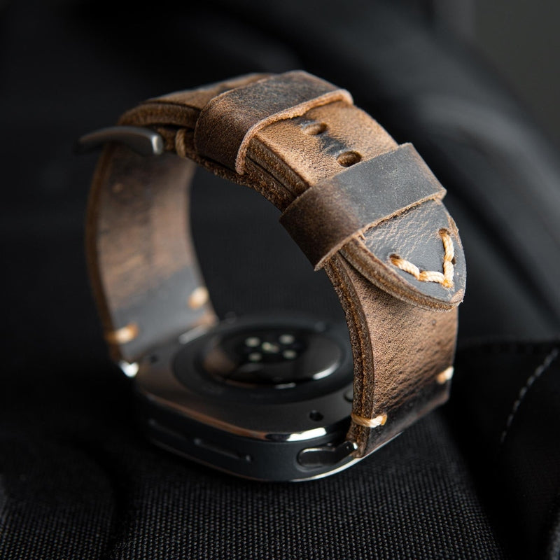 Macro detail of curved brown leather strap loop with rough texture and V-stitch