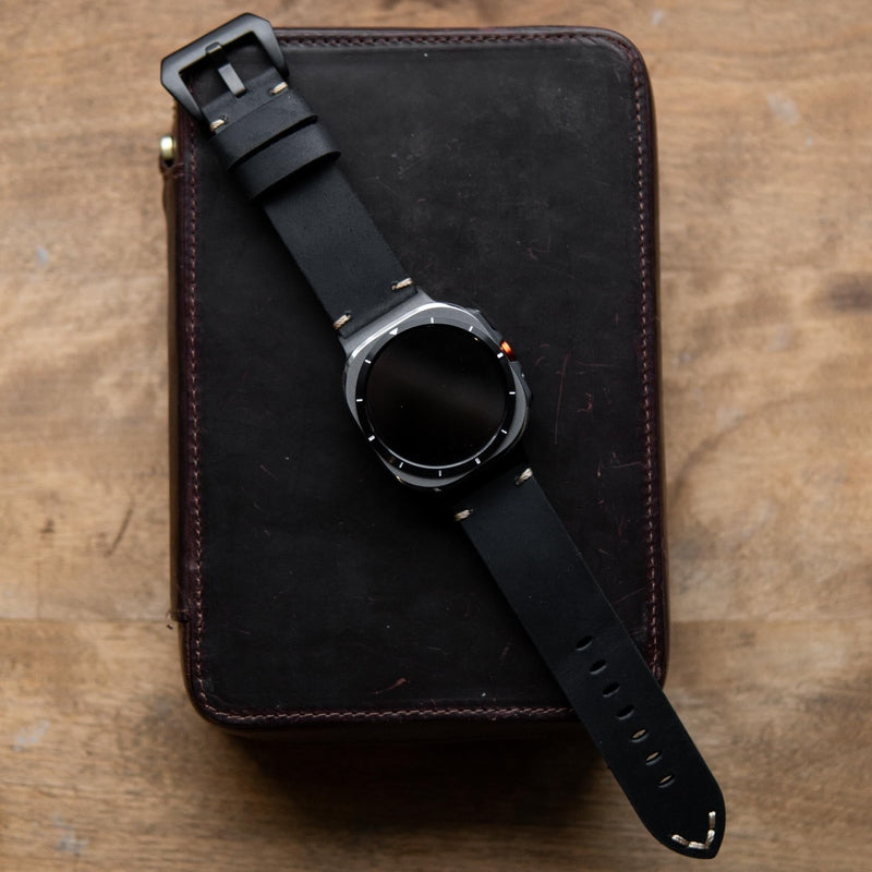Black leather watch band with silver hardware on wooden table