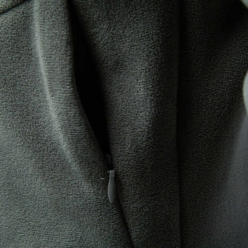 Detail of dark grey-green fabric zipper pull tab at base of half-collar neck opening