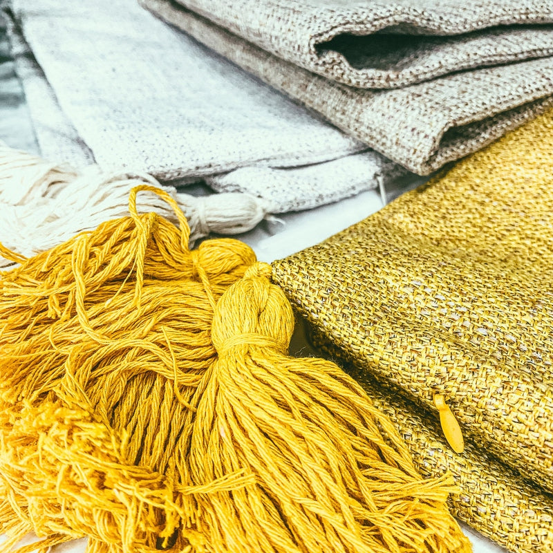 Close-up of yellow tassel and grey gold woven texture on folded cotton linen pillow case