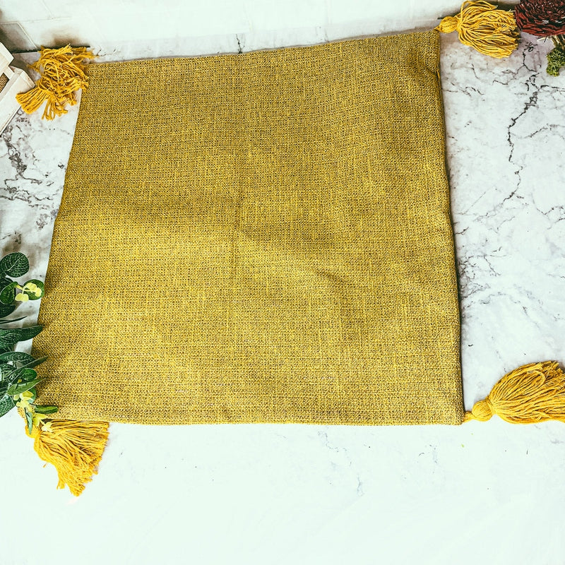 Mustard yellow square pillow case with corner tassels on white marble surface