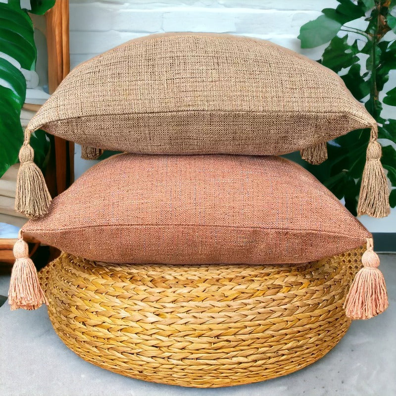 Stacked tan and terracotta boho cotton linen pillow cases with tassels on rattan ottoman