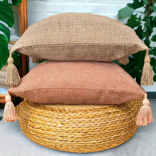 Stacked tan and terracotta boho cotton linen pillow cases with tassels on rattan ottoman