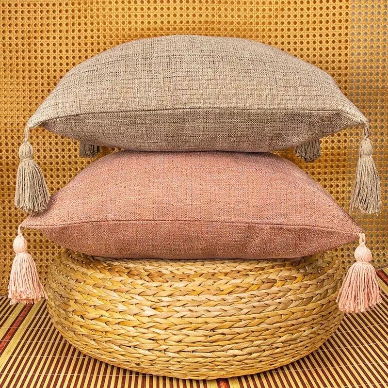 Beige and dusty rose stacked pillow cases with tassels on seagrass basket