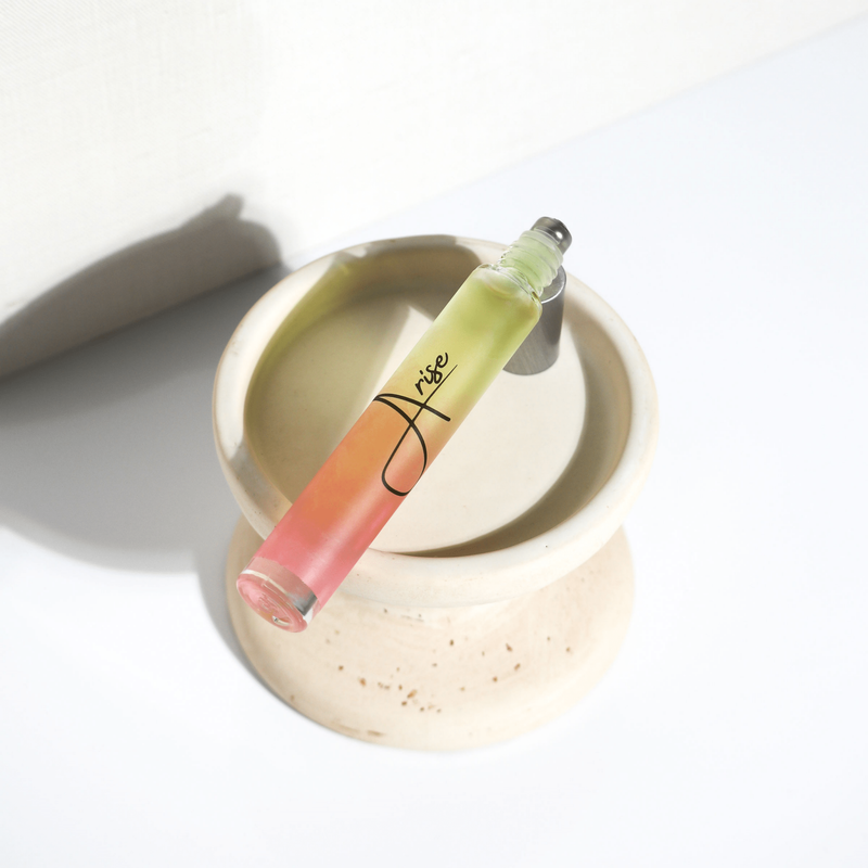 Arise rollerball perfume bottle with pink and green gradient liquid in beige dish