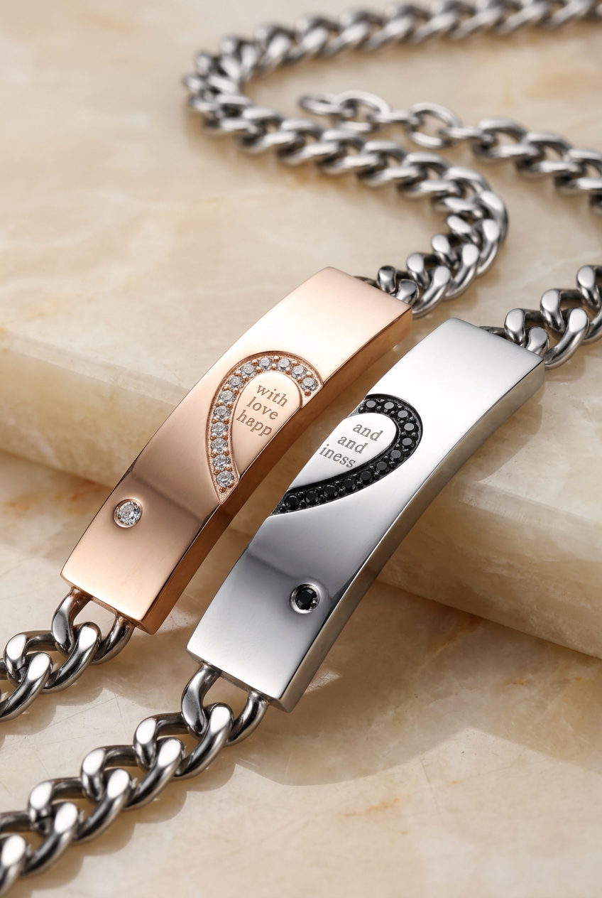 Close-up of couple bracelet plates with engraved half-heart motifs, clear and black stones, and silver-tone curb chains.