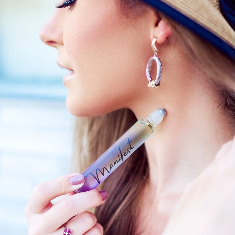 Woman applying Manifest rollerball perfume to neck for on-the-go fragrance touch-up